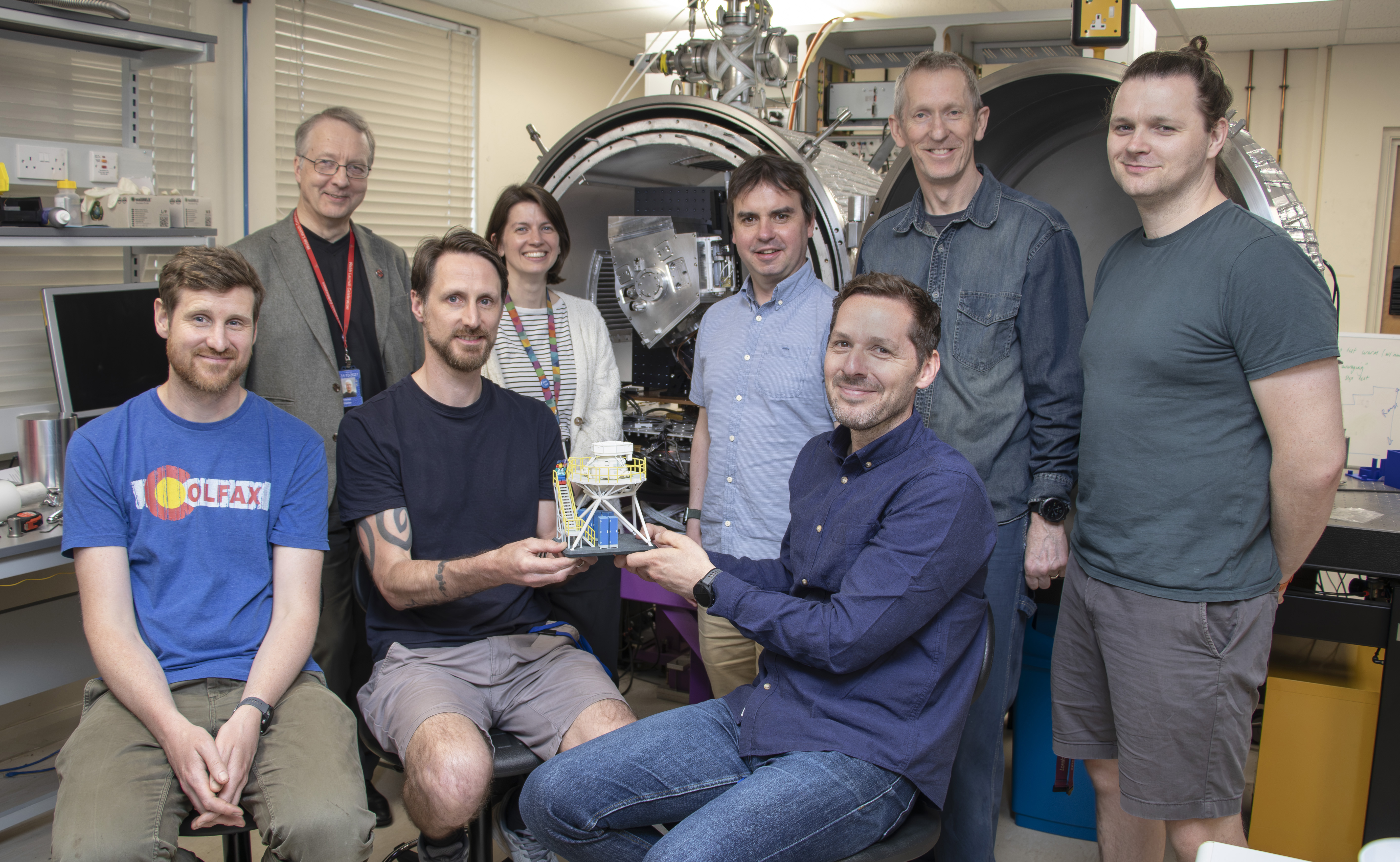The 8-person UK ATC team working on METIS pictureed in the lab holding up a scale model of the instrument.