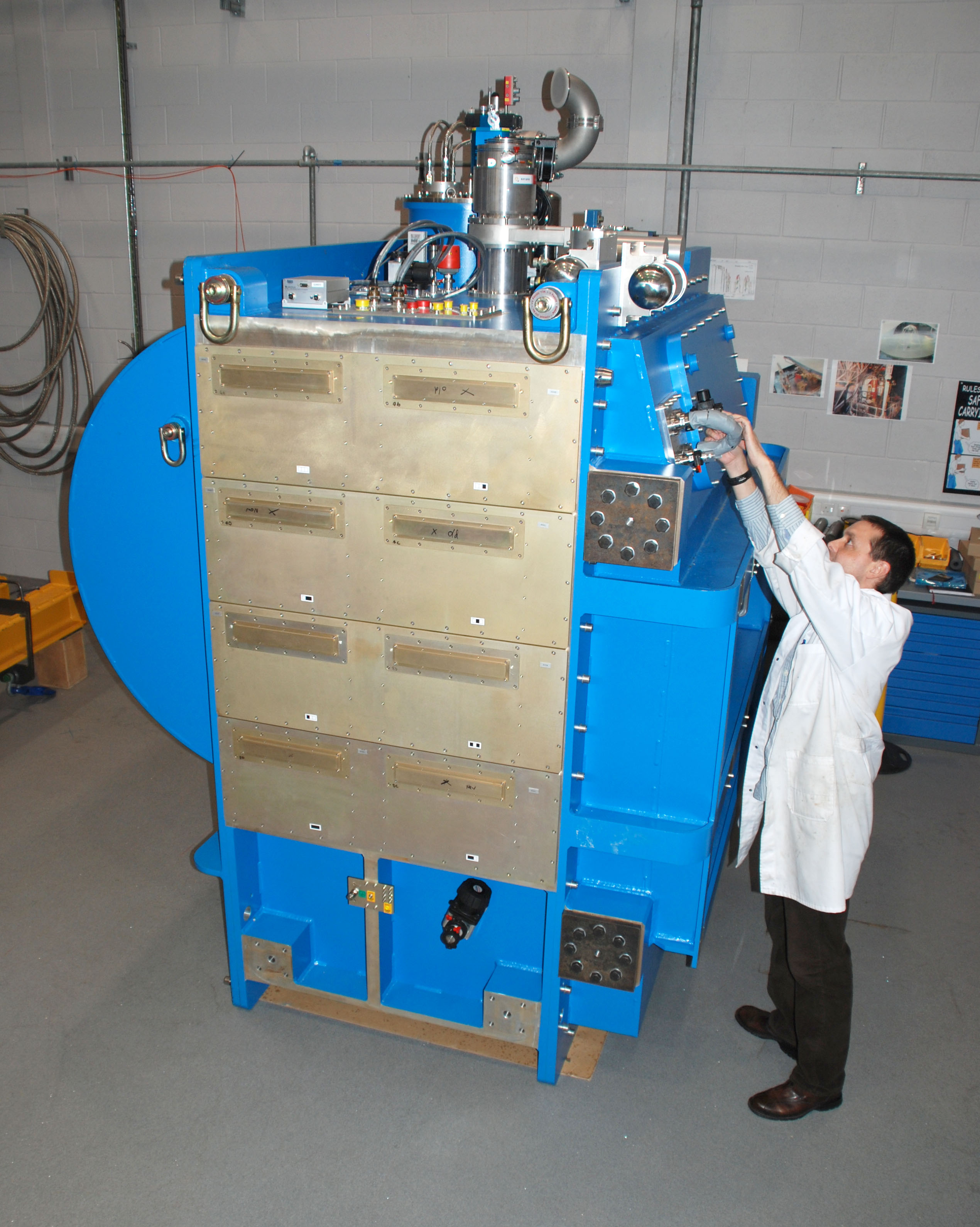 A scientist makes adjustments to SCUBA 2, which is a large blue and metal astronomical instrument, in the lab at UK ATC.